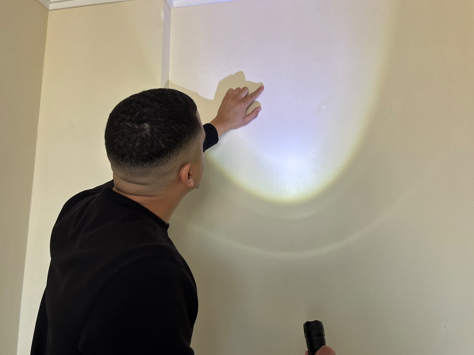 Alex inspecionando a superfície de uma parede com uma lanterna